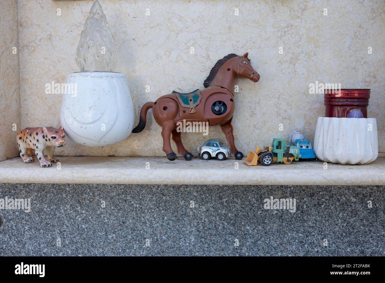 Jouet, cassé, cheval mécanique avec 3 pattes, voitures jouets sur une tombe d'urne dans un cimetière, Bari Sardo, Ogliastra, Sardaigne, Italie Banque D'Images