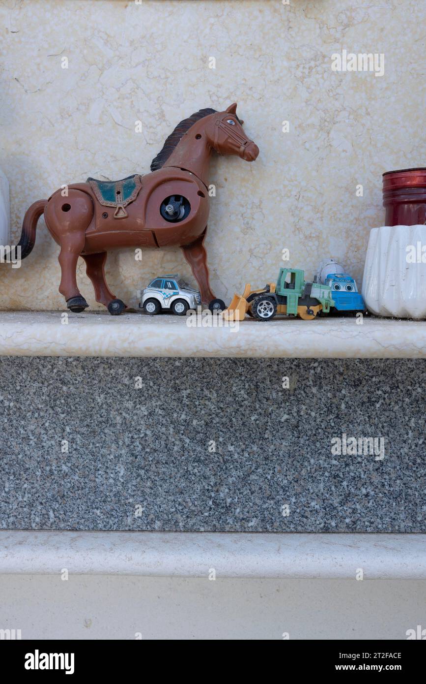 Jouet, cassé, cheval mécanique avec 3 pattes, voitures jouets sur une tombe d'urne dans un cimetière, Bari Sardo, Ogliastra, Sardaigne, Italie Banque D'Images