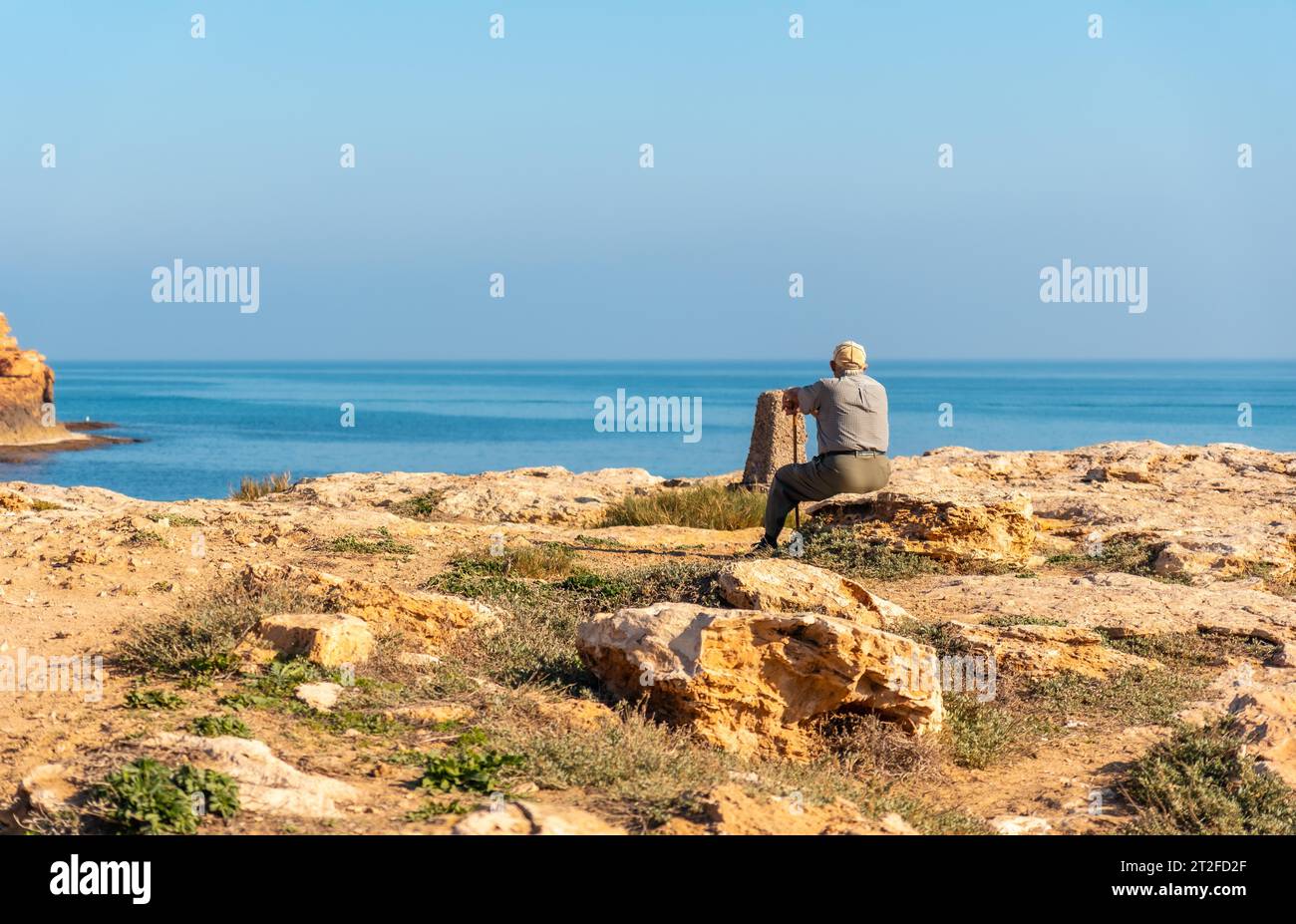 Bel endroit où est un vieil homme pensif avec un béret assis et avec une canne sur la côte regardant la mer. seigneur traditionnel de la culture espagnole Banque D'Images