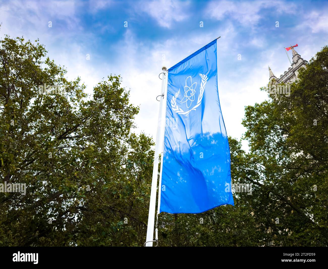 Le logo de l'Agence internationale de l'énergie atomique (AIEA) sur un drapeau bleu volant à côté d'arbres à l'extérieur du Queen Elizabeth II Centre à Londres, Royaume-Uni. Banque D'Images