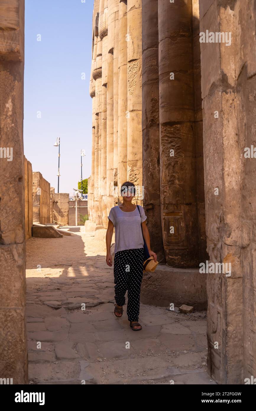 Un jeune touriste dans un t-shirt blanc et chapeau visitant le temple et regardant les dessins égyptiens antiques sur les colonnes du temple de Louxor, Egypte, Banque D'Images