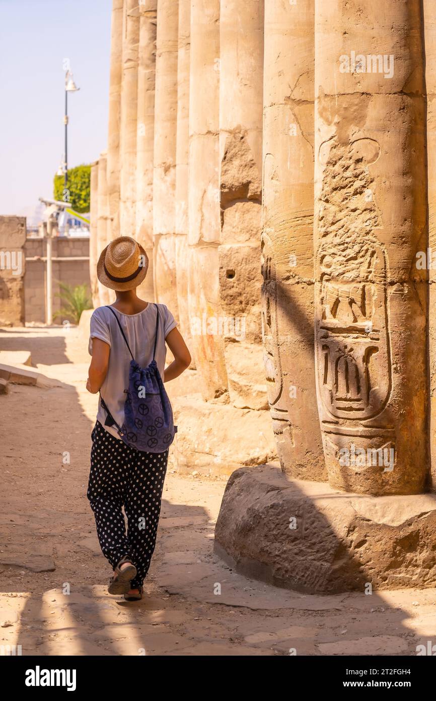 Un jeune touriste dans un t-shirt blanc et chapeau visitant le temple et regardant les anciens dessins égyptiens sur les colonnes du temple de Louxor, en Égypte Banque D'Images