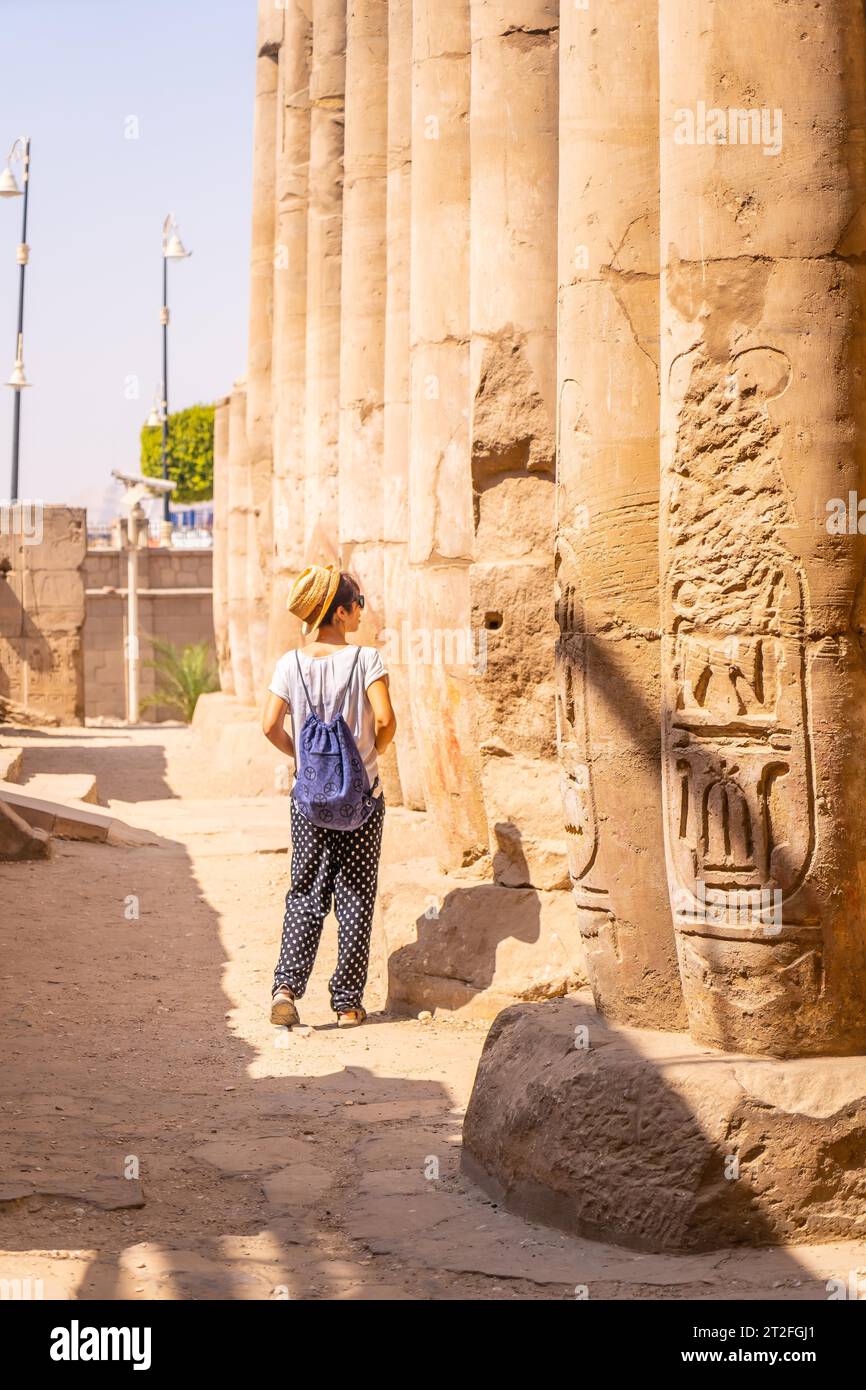 Un jeune touriste dans un t-shirt blanc et chapeau visitant le temple et regardant les anciens dessins égyptiens sur les colonnes du temple de Louxor, en Égypte Banque D'Images