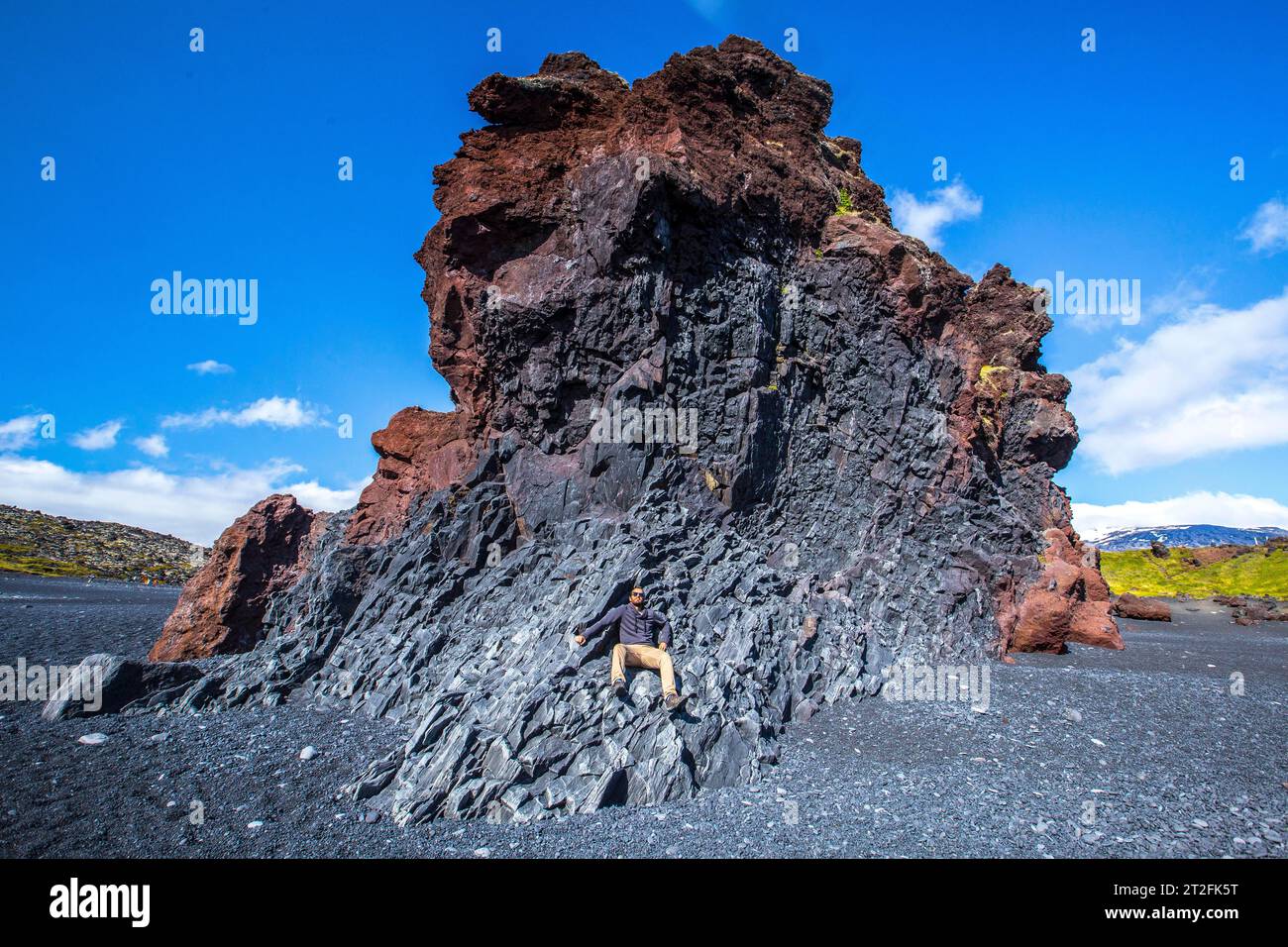 Un jeune homme au sommet de quelques rochers assis sur la plage noire de la côte de Snaefellsnes. Islande Banque D'Images