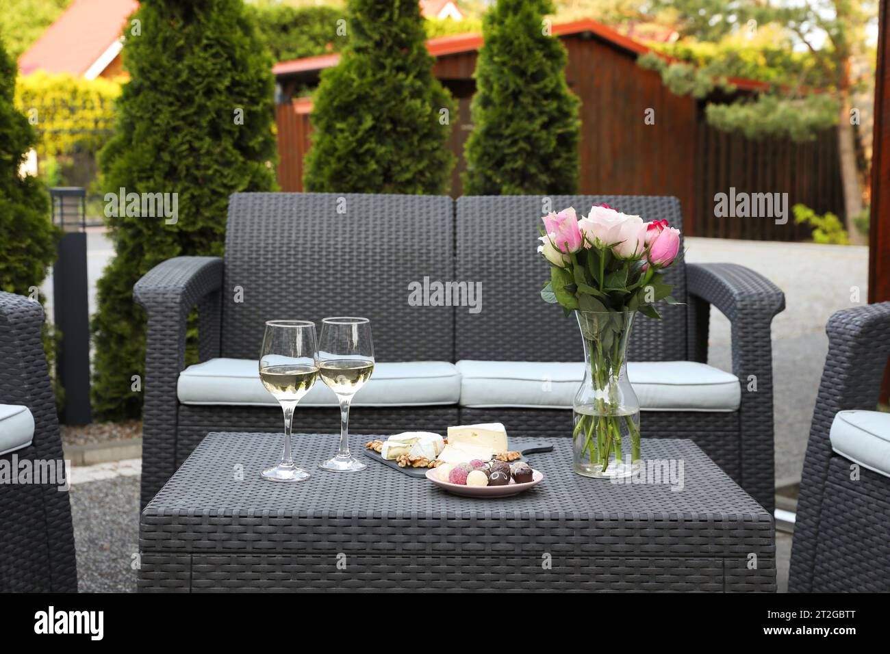 Vase avec des roses, des verres de vin et de la nourriture sur la table en rotin sur la terrasse extérieure Banque D'Images