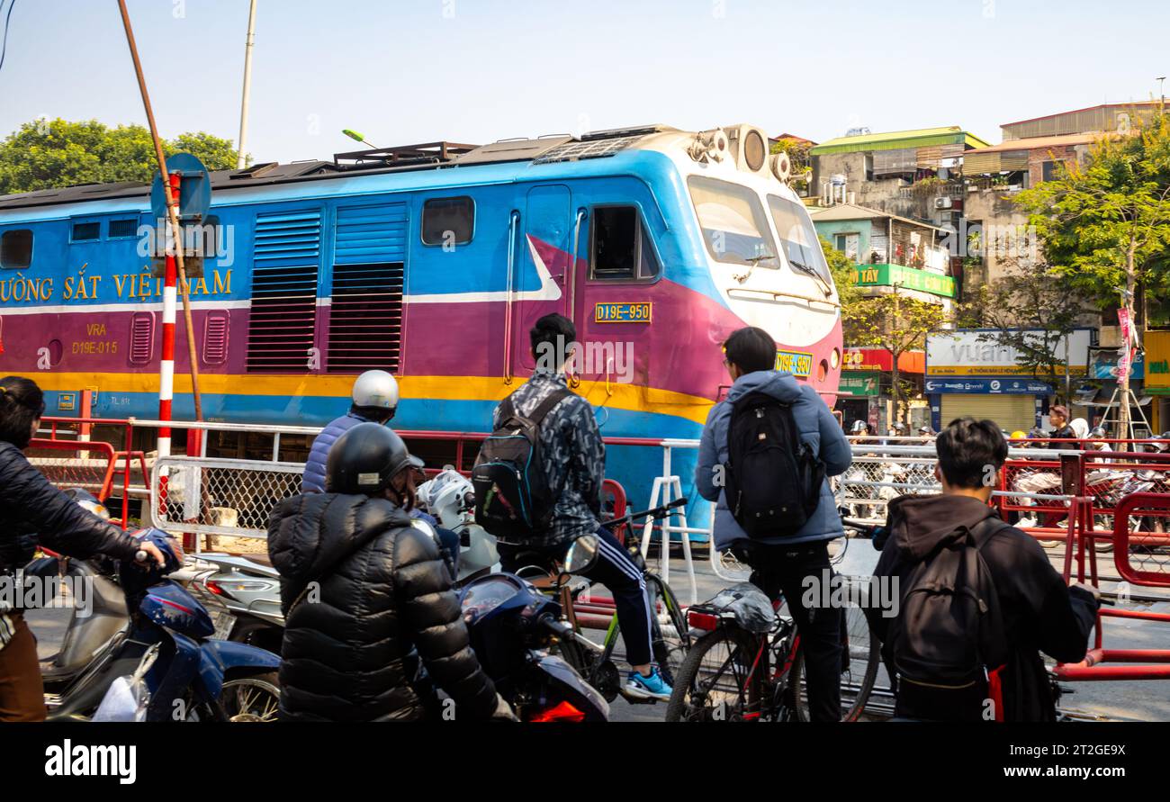 Un train des chemins de fer du Vietnam passe des gens à moto et à vélo à un passage à niveau (passage à niveau) à Hanoi, Vietnam. Banque D'Images Un train des chemins de fer du Vietnam passe des gens à moto et à vélo à un passage à niveau (passage à niveau) à Hanoi, Vietnam. Banque D'Images