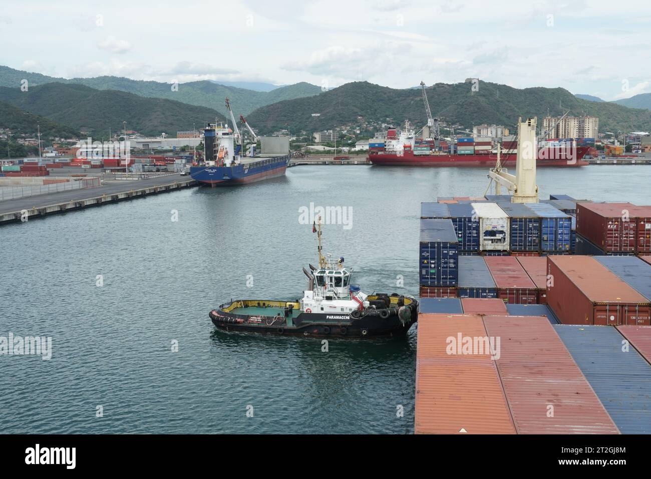 Porte-conteneurs avec grue quittant le port avec l ' aide d ' un remorqueur qui pousse la proue. Banque D'Images