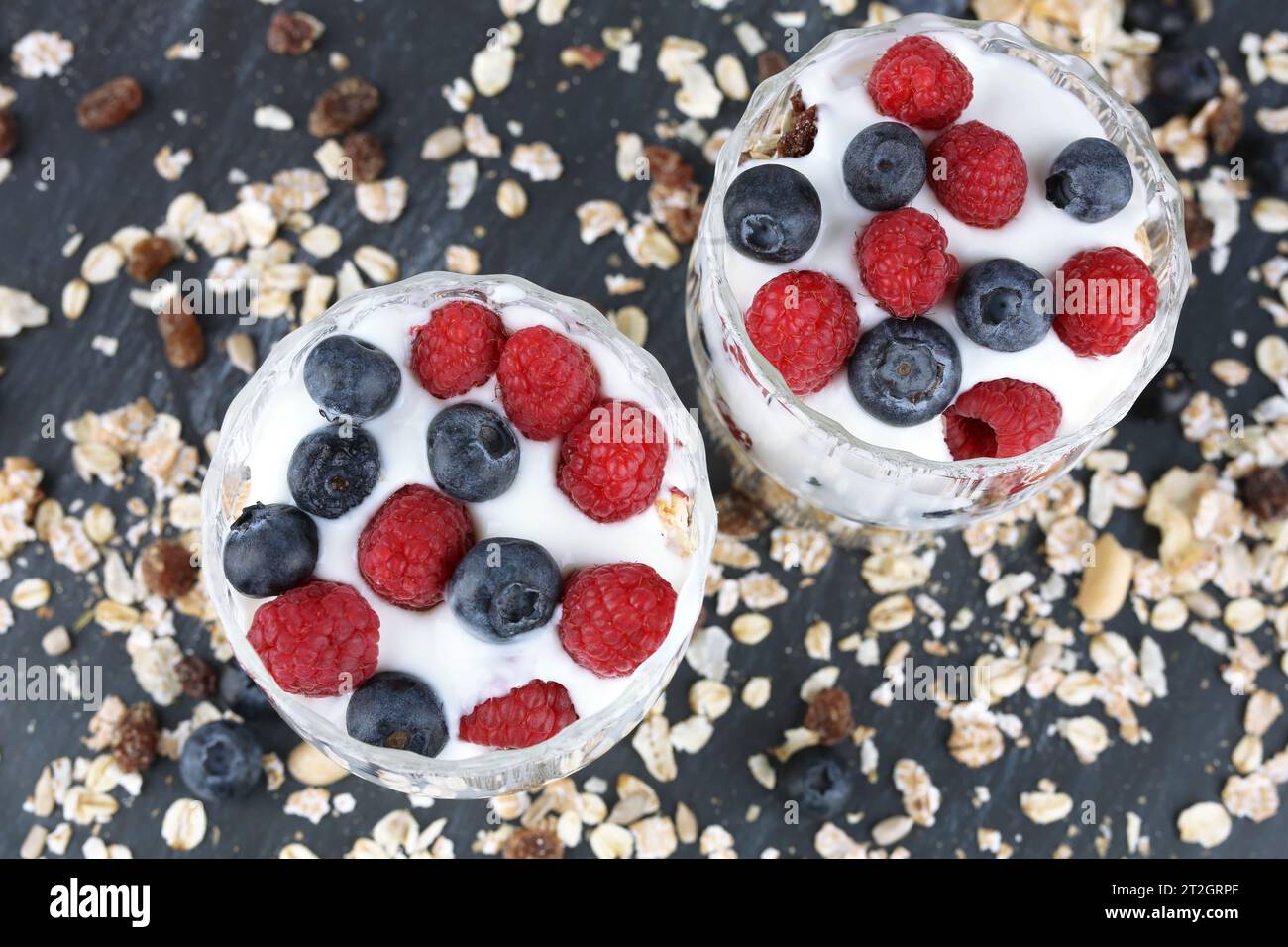 Muesly avec des framboises et des bleuets dans deux verres sur fond sombre. Banque D'Images