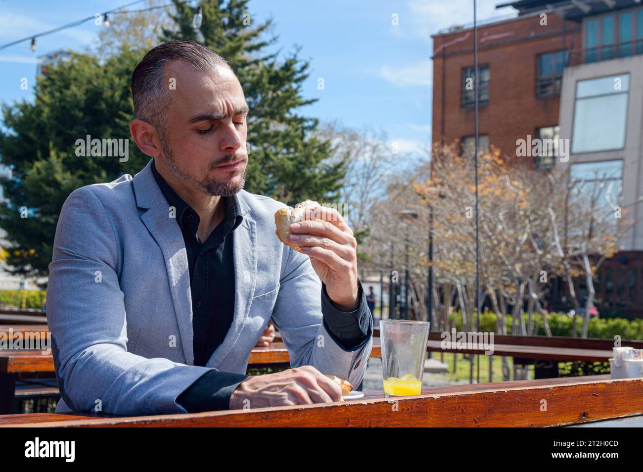 Homme caucasien adulte, assis à l'extérieur du restaurant, appréciant la journée heureuse de voir comment délicieux sandwich il mange. espace de copie. Banque D'Images