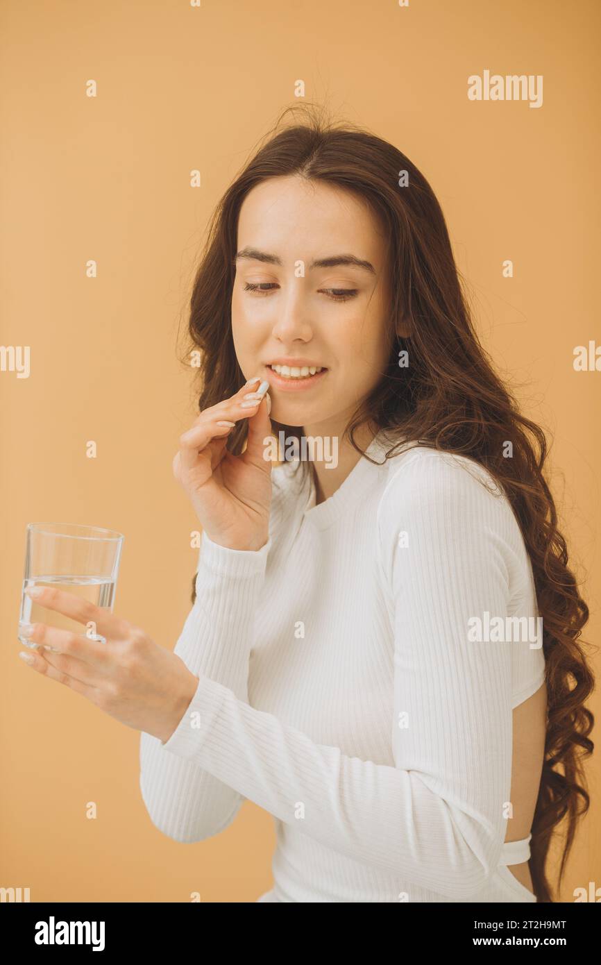 Jolie jeune femme prenant des vitamines. Une femme tient une pilule et un verre d'eau. Banque D'Images