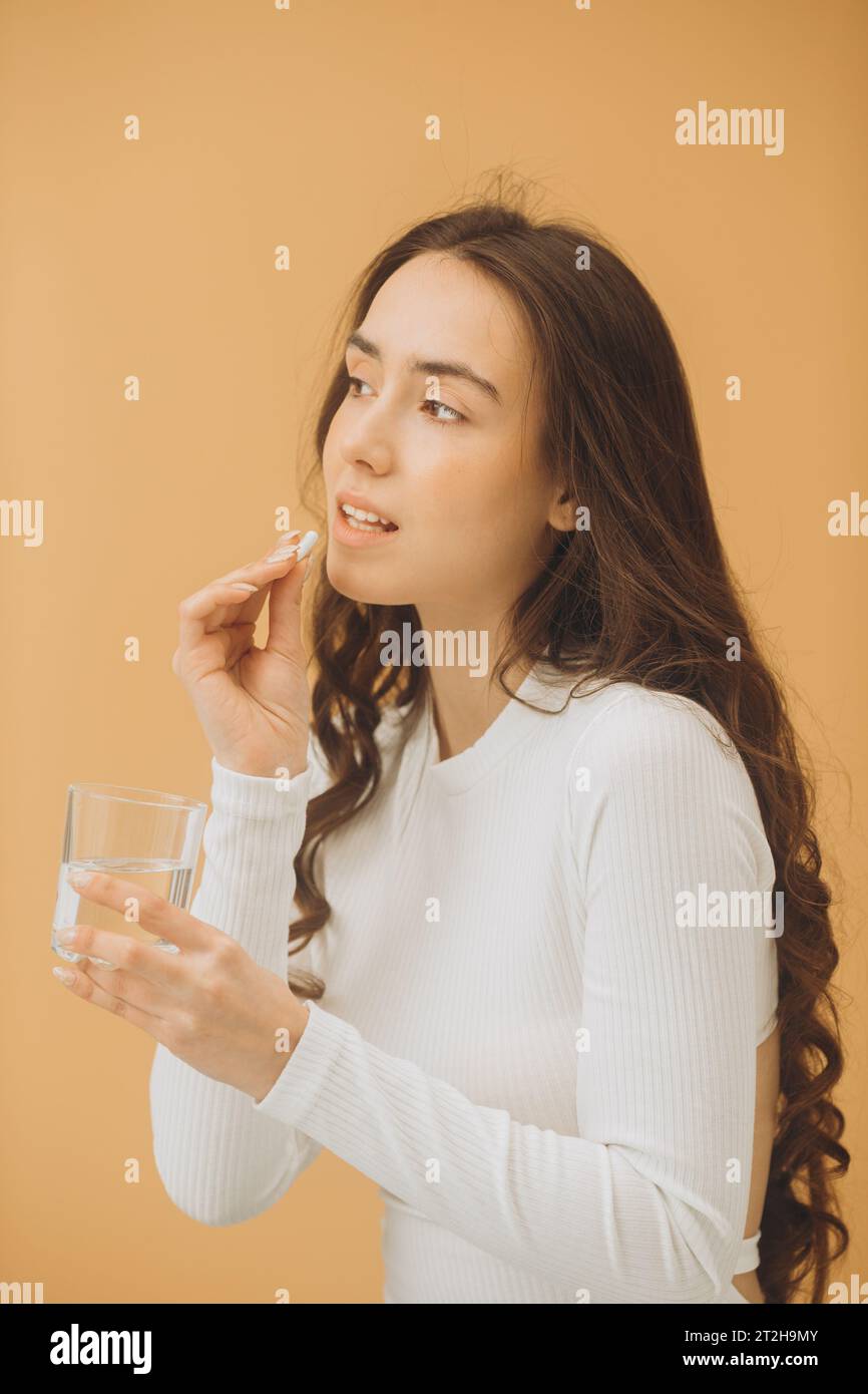 Jolie jeune femme prenant des vitamines. Une femme tient une pilule et un verre d'eau. Banque D'Images