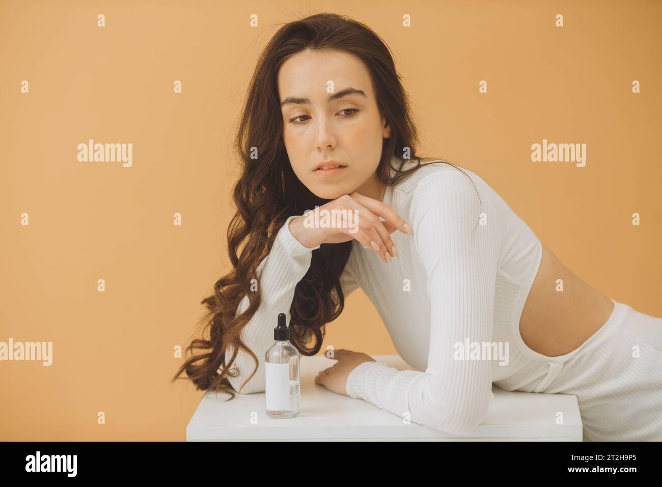 Une belle fille avec une bouteille d'eau micellaire ou d'autres cosmétiques pose sur un fond beige. Le concept de beauté et de soins de la peau. Banque D'Images