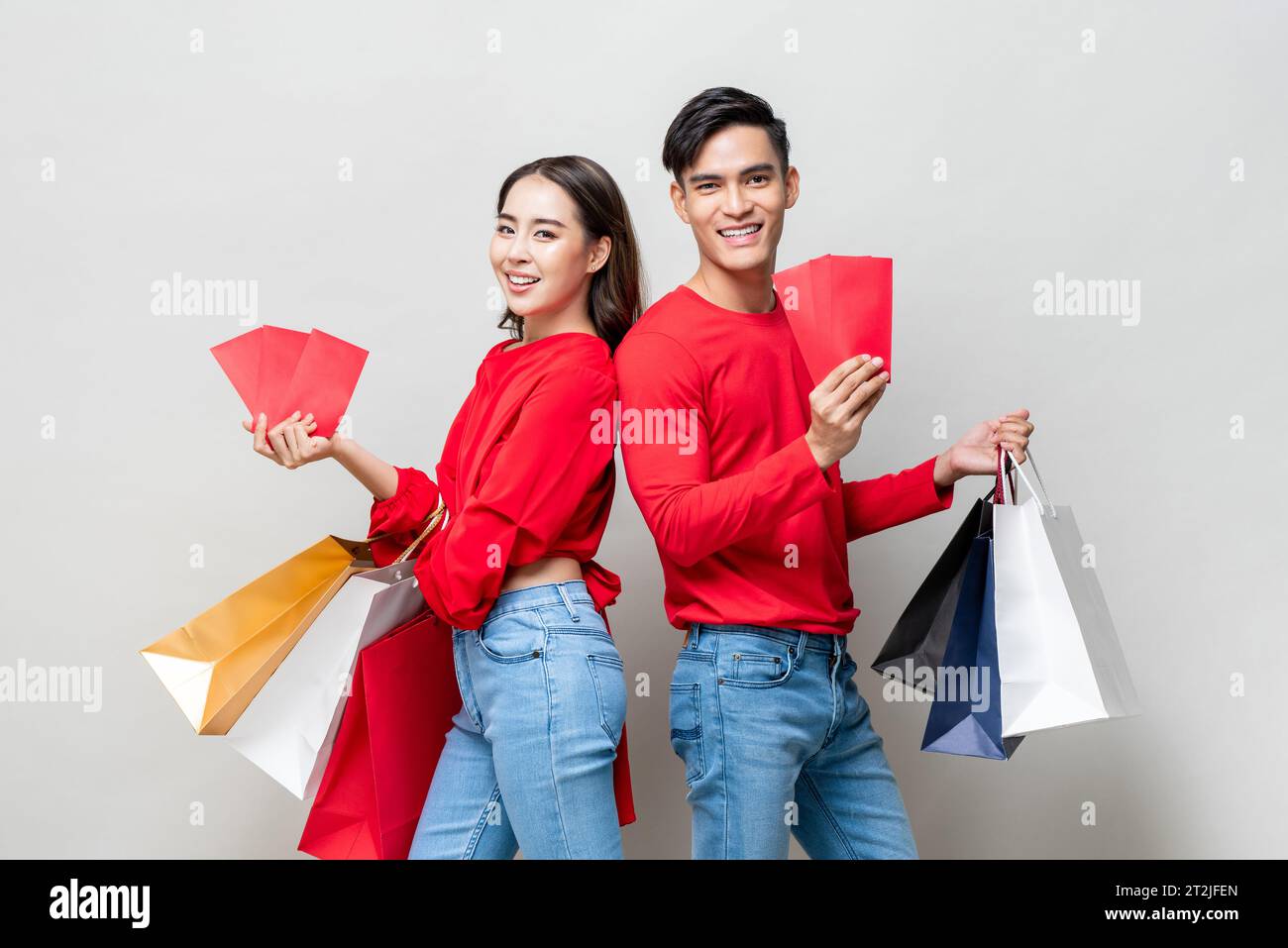 Couple asiatique heureux avec sacs de shopping et enveloppes rouges isolées En studio gris pour le concept chinois de vente du nouvel an Banque D'Images