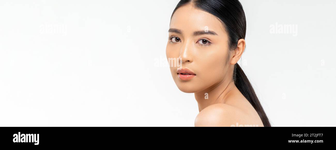 Séduisante jeune femme asiatique avec la peau propre regardant la caméra sur l'épaule pendant la routine de beauté sur fond blanc Banque D'Images