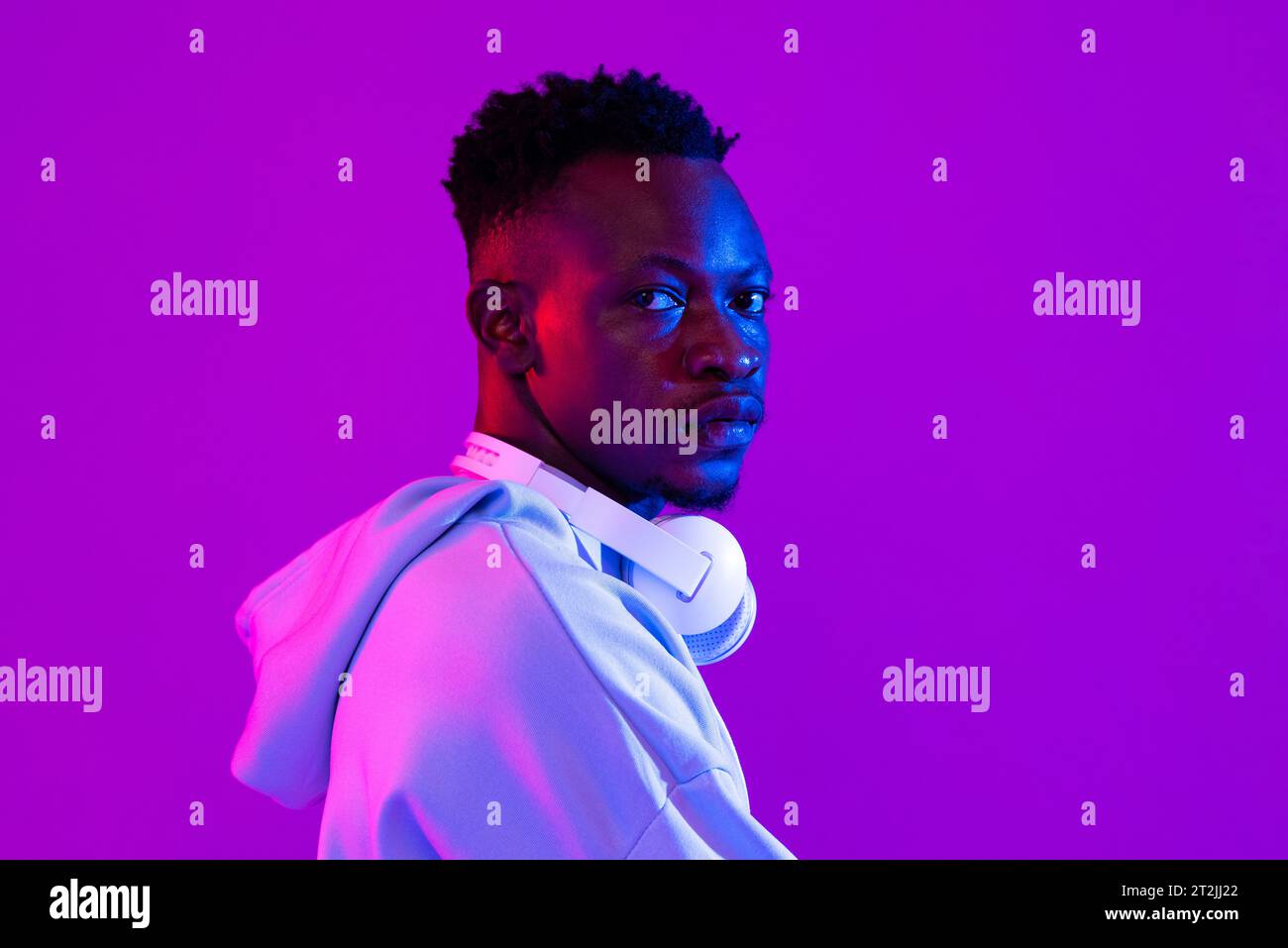 Portrait de jeune homme africain avec des écouteurs dans le fond de studio de lumière néon Banque D'Images