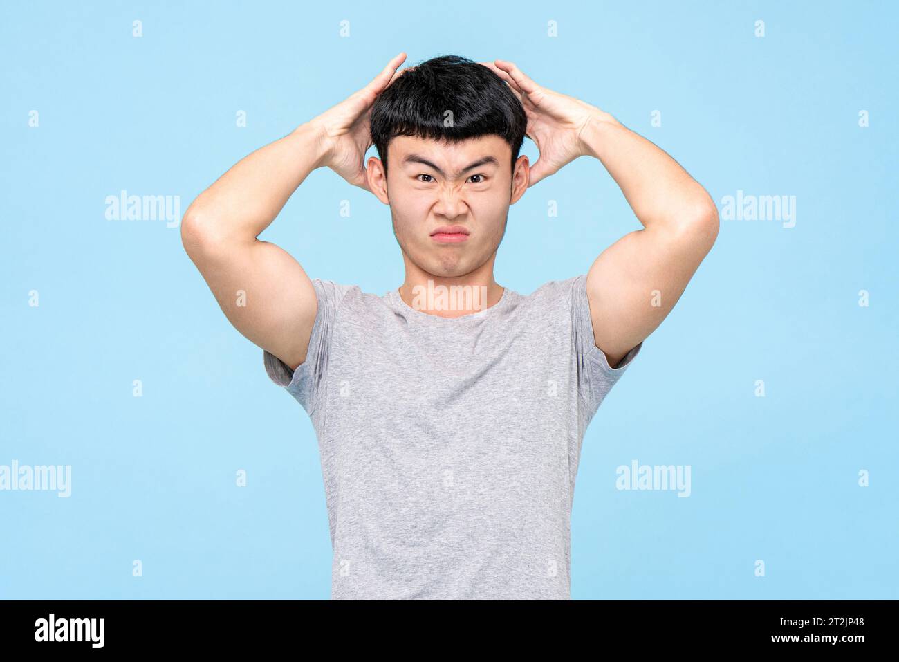 Mécontentement homme asiatique touchant la tête avec une expression furieuse tout en se tenant sur fond bleu clair isolé dans le studio Banque D'Images