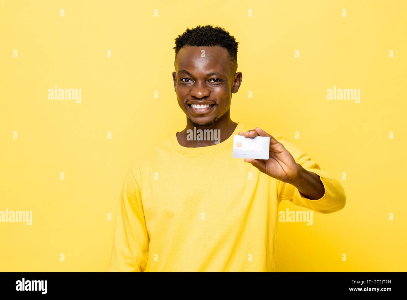 Homme africain souriant en tenue décontractée tenant une carte de crédit sur fond jaune isolé de studio Banque D'Images