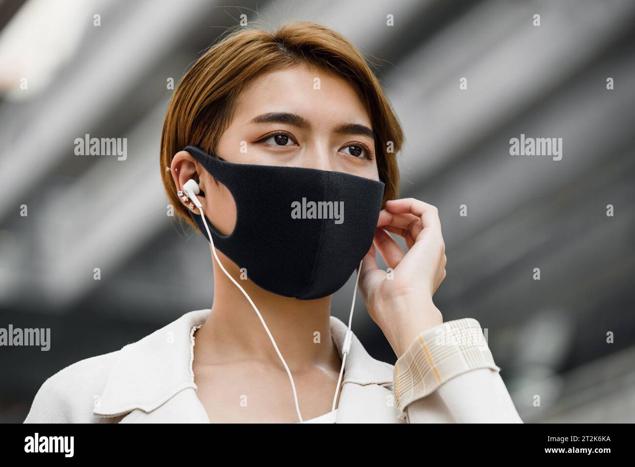 Jeune femme asiatique portant un masque facial à l’extérieur tout en écoutant de la musique dans la ville pendant la pandémie de COVID-19 Banque D'Images