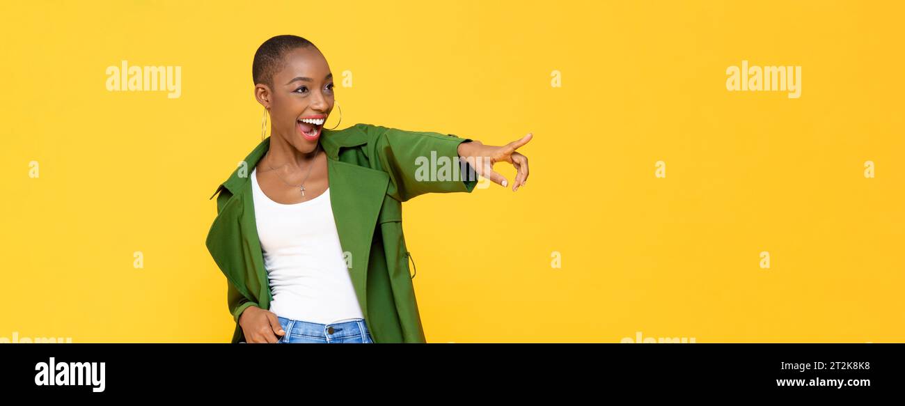 Tendance jeune femme afro-américaine souriante et pointant la main sur le côté pour copier l'espace dans le fond de bannière isolé de studio de couleur jaune Banque D'Images