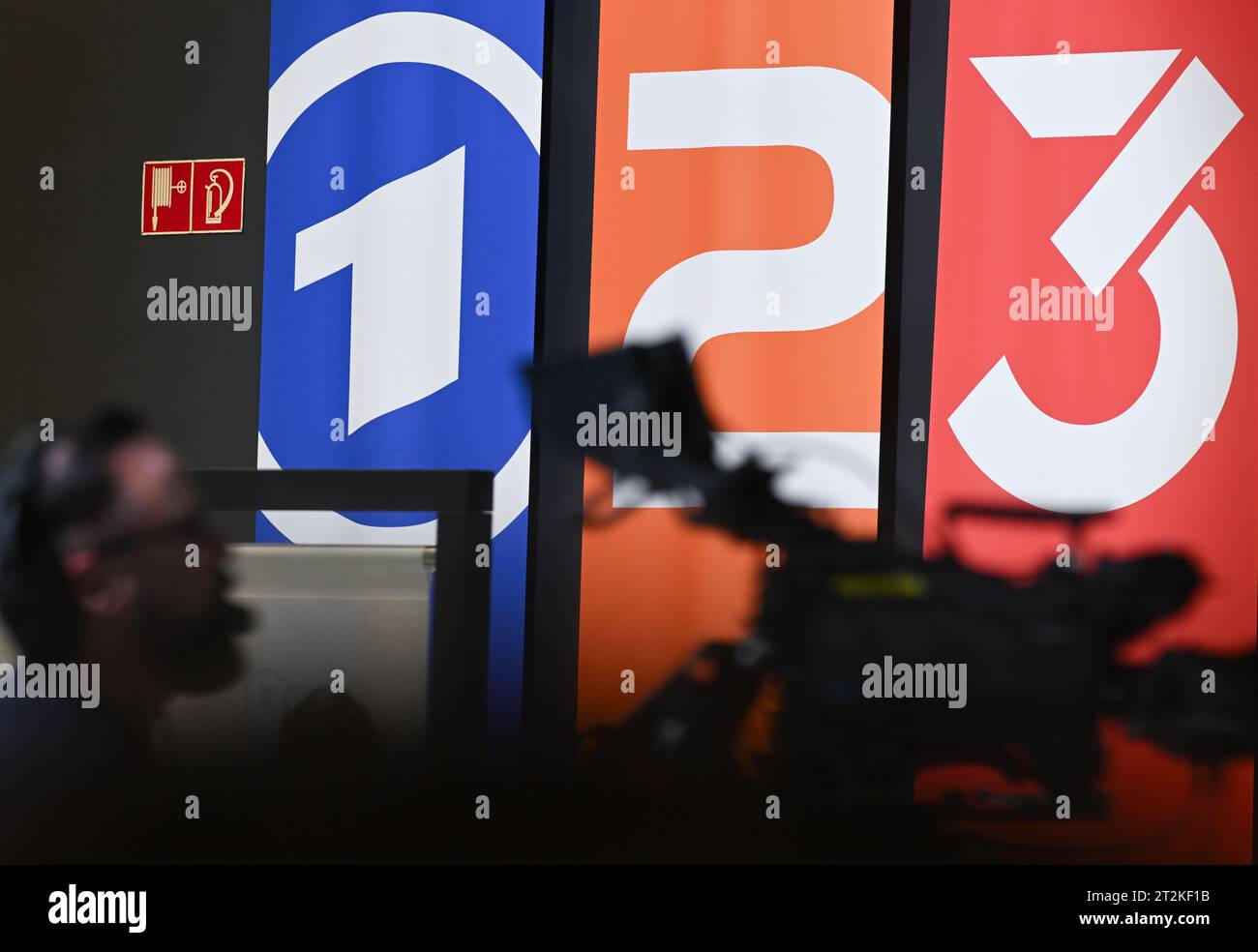 20 octobre 2023, Hesse, Frankfurt/main : les drapeaux avec les logos de la marque ARD (Das Erste, l-r), ZDF (Zweites Deutsches Fernsehen) et 3Rors sont vus en arrière-plan d'une caméra de télévision à la Foire du livre de Francfort. Photo : Arne Dedert/dpa Banque D'Images