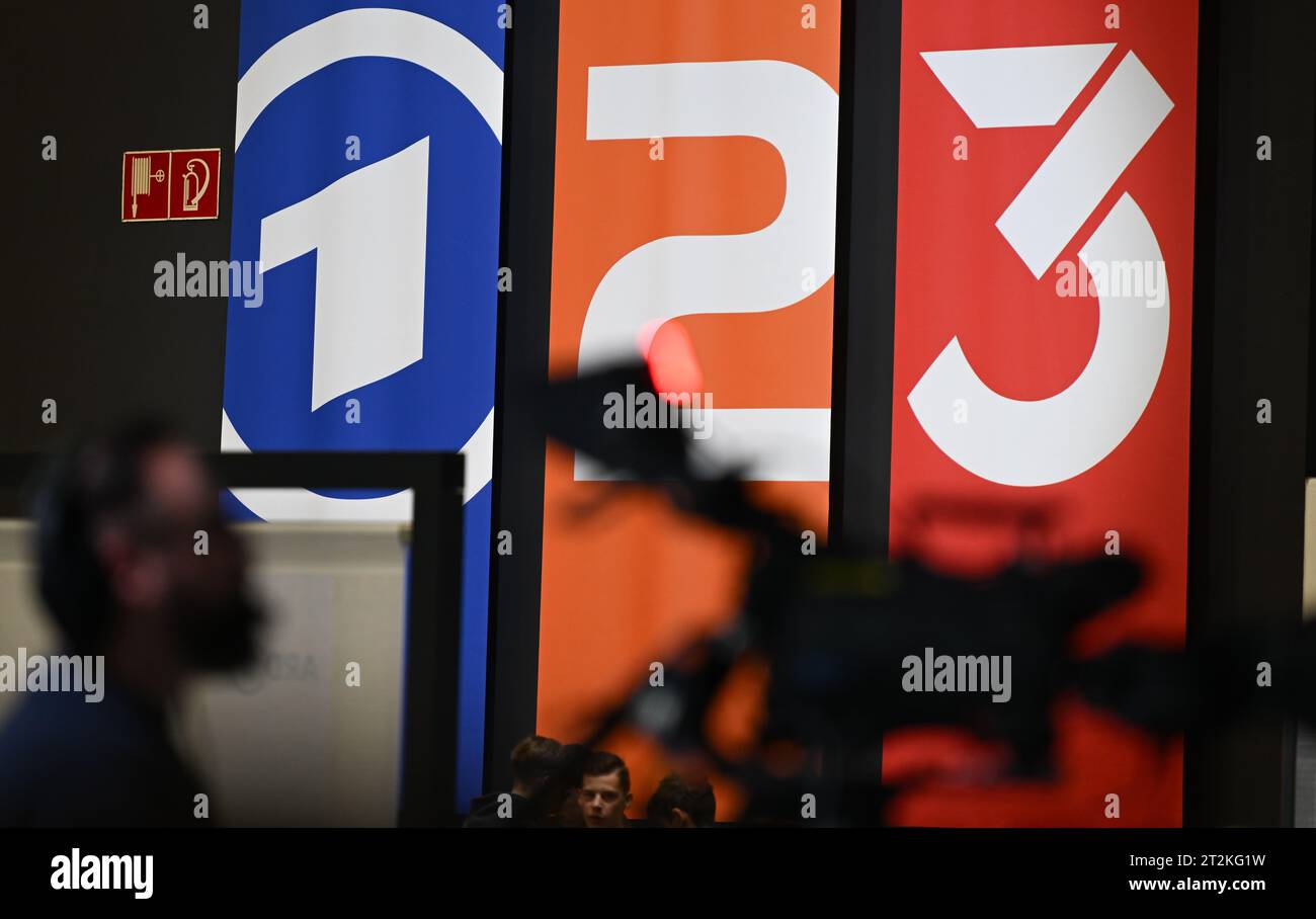 20 octobre 2023, Hesse, Frankfurt/main : les drapeaux avec les logos de la marque ARD (Das Erste, l-r), ZDF (Zweites Deutsches Fernsehen) et 3Rors sont vus en arrière-plan d'une caméra de télévision à la Foire du livre de Francfort. Photo : Arne Dedert/dpa Banque D'Images