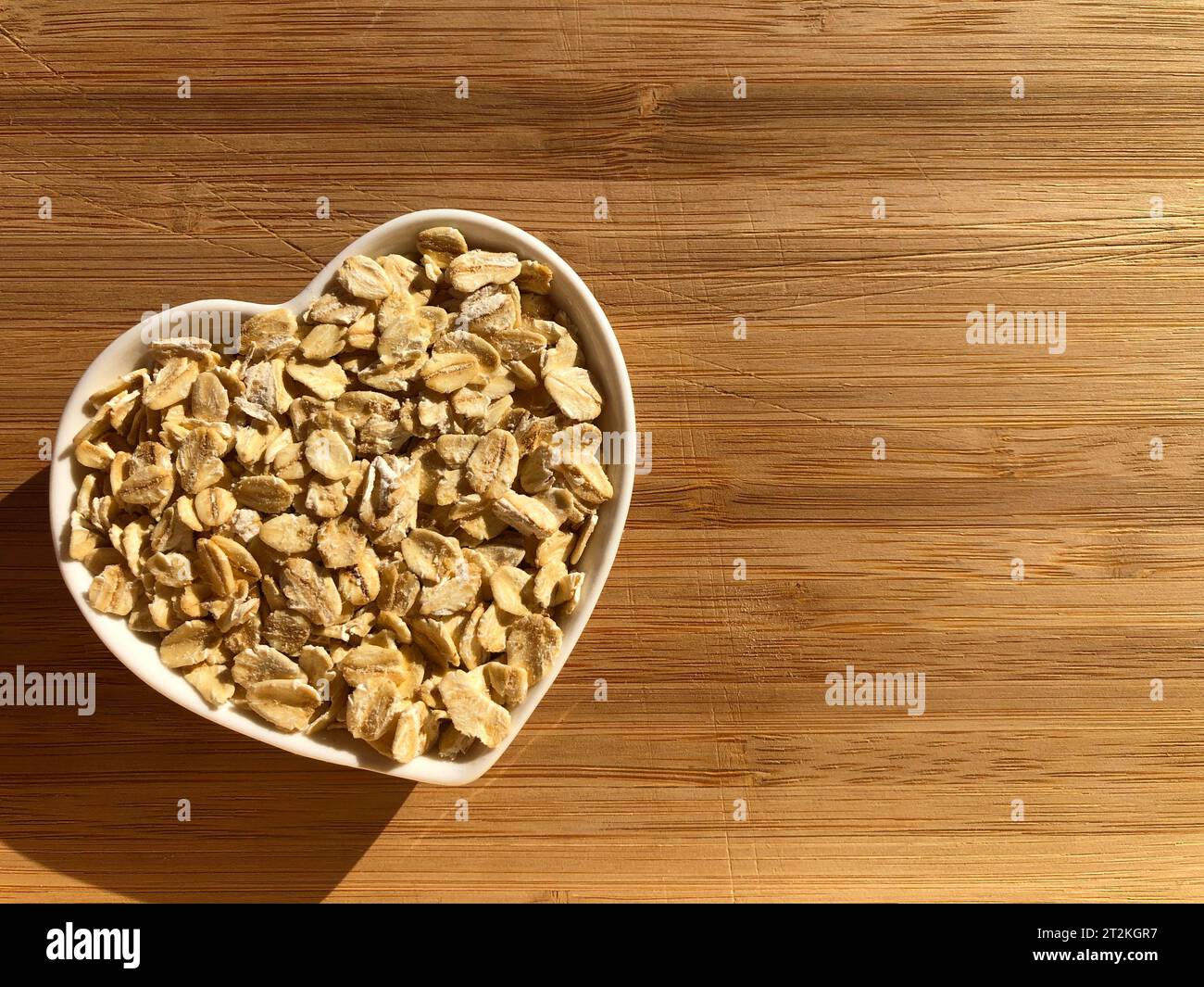 Concept créatif : alimentation saine, coeur sain. Flocons d'avoine dans un plat en forme de coeur isolé sur un fond de bois avec espace de copie Banque D'Images