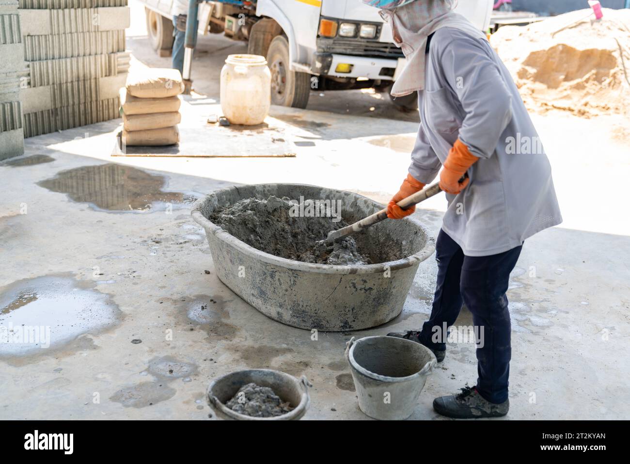 Travailleur mélanger manuellement la poudre de ciment, le sable, les pierres dans le bassin pour mélanger le ciment dans le chantier de construction. Banque D'Images