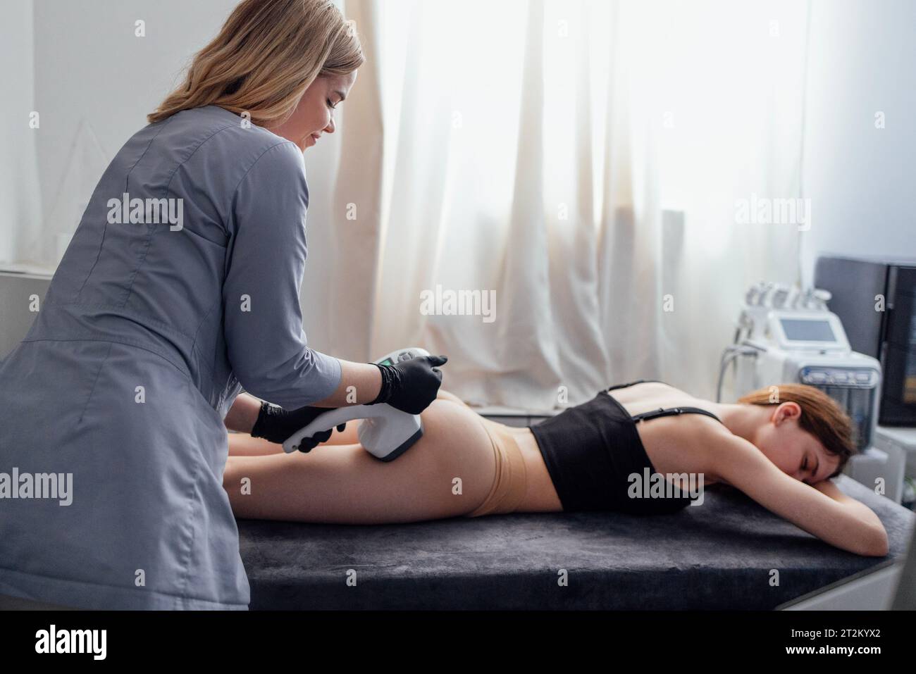 Masseuse souriante fait du matériel anti-cellulite massage fesses à son client. Jeune femme se couche sur la table de massage et reçoit le procédé de drainage lymphatique Banque D'Images