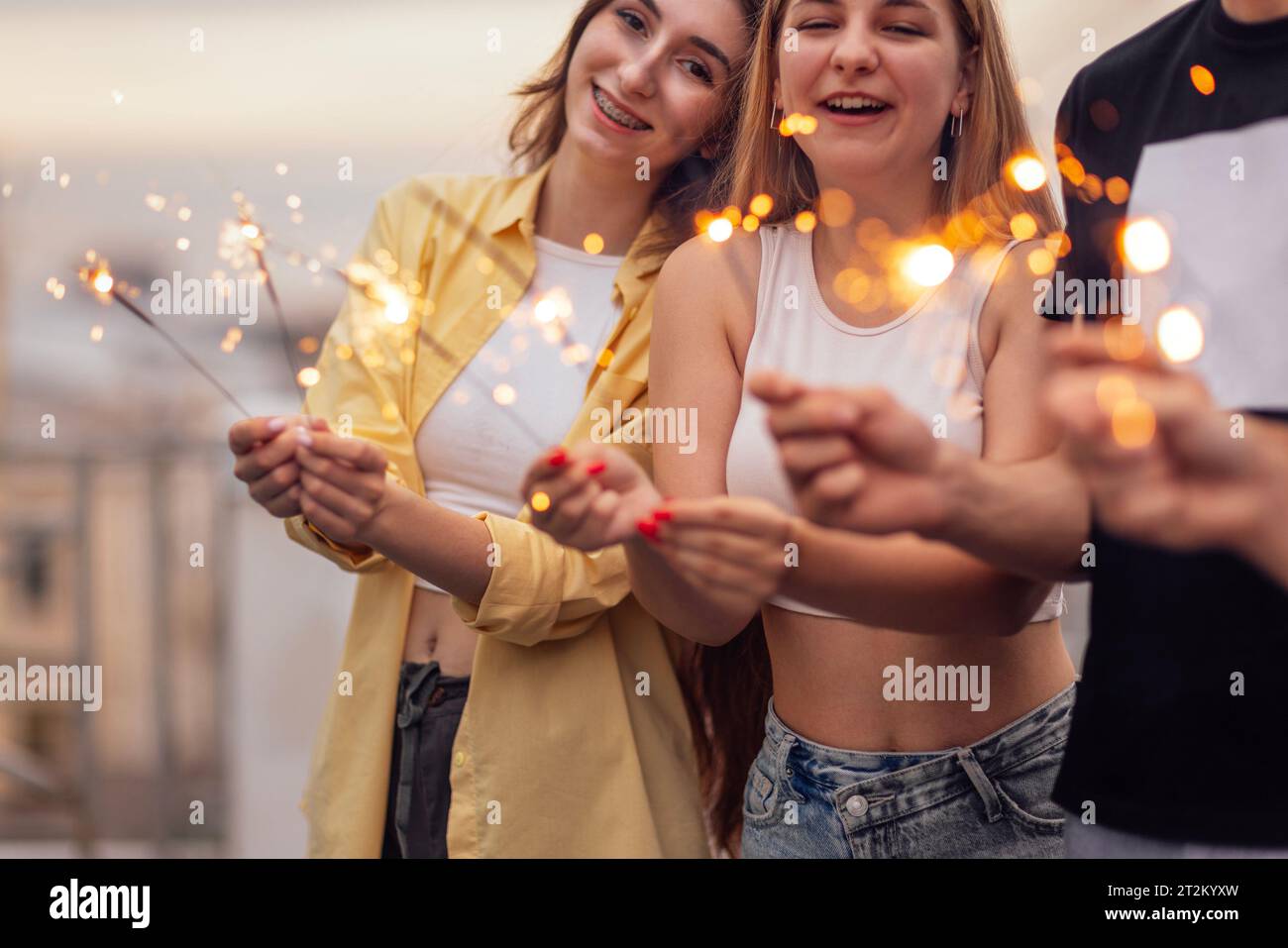 Deux gars mignons et deux filles charmantes tiennent des étincelles et sourient. Les amis en vêtements décontractés s'amusent et rient. Quatre adolescents célèbrent un rendez-vous Banque D'Images