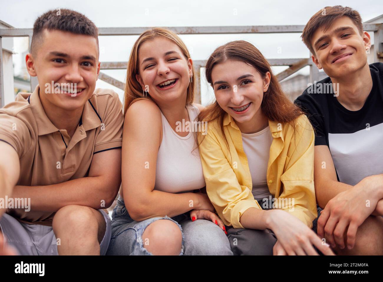 Quatre adolescents mignons prenant un selfie. Funny Friends prend une photo de soi-même sur le téléphone à l'extérieur. Garçons et filles souriants assis dans la rue. Ha Banque D'Images