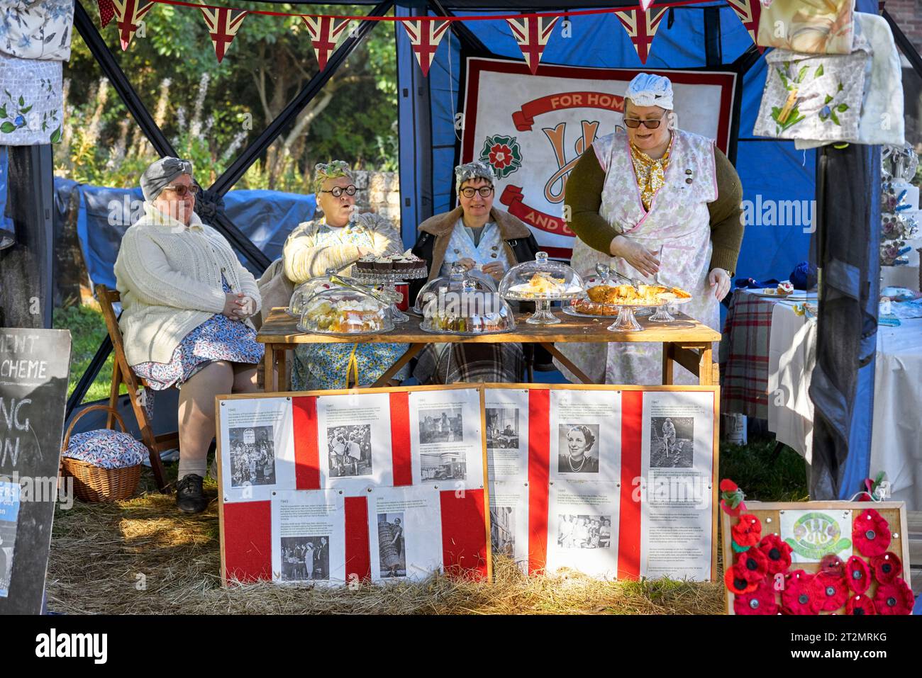 Reconstitution des années 1940 avec des femmes aînées anglaises habillées en tenue des années 1940 et servant des gâteaux d'un étal de nourriture. Angleterre Royaume-Uni Banque D'Images