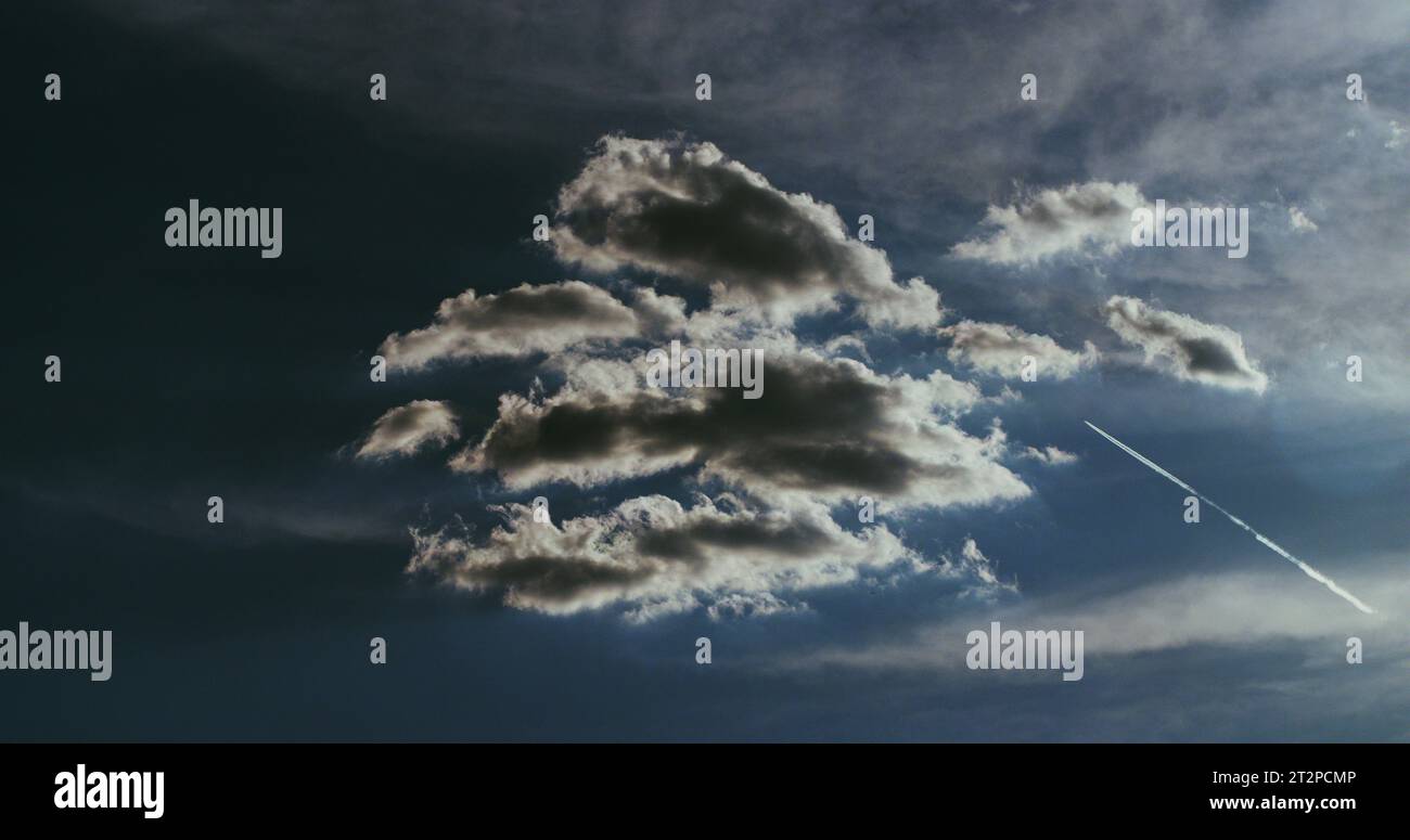 Paysage nuageux hypnotique sous un ciel bleu profond et un avion à réaction qui tranche à travers le ciel laissant une traînée de condensation blanche pure. Banque D'Images
