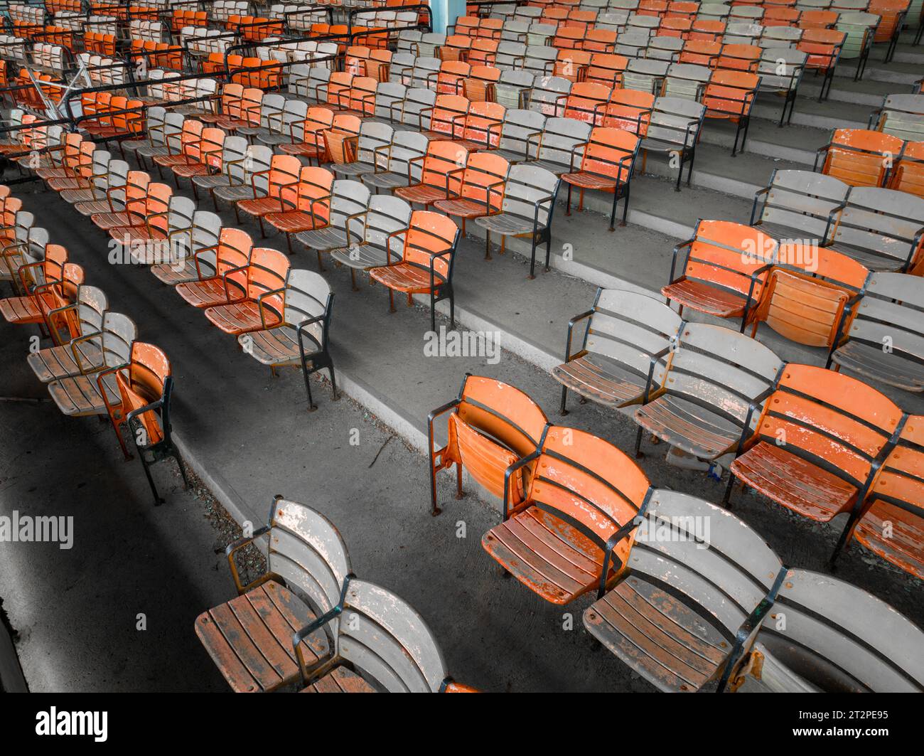 Vieux sièges en bois peints orange et jaune délavé dans une tribune abandonnée d'un stade. Banque D'Images