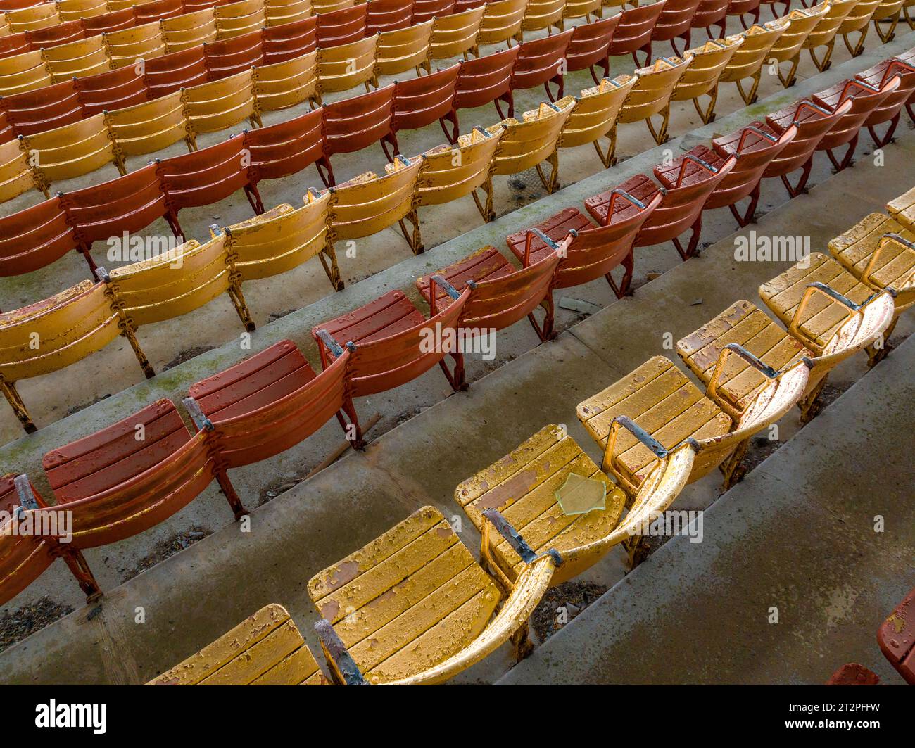 Vieux sièges en bois peints orange et jaune délavé dans une tribune abandonnée d'un stade. Banque D'Images