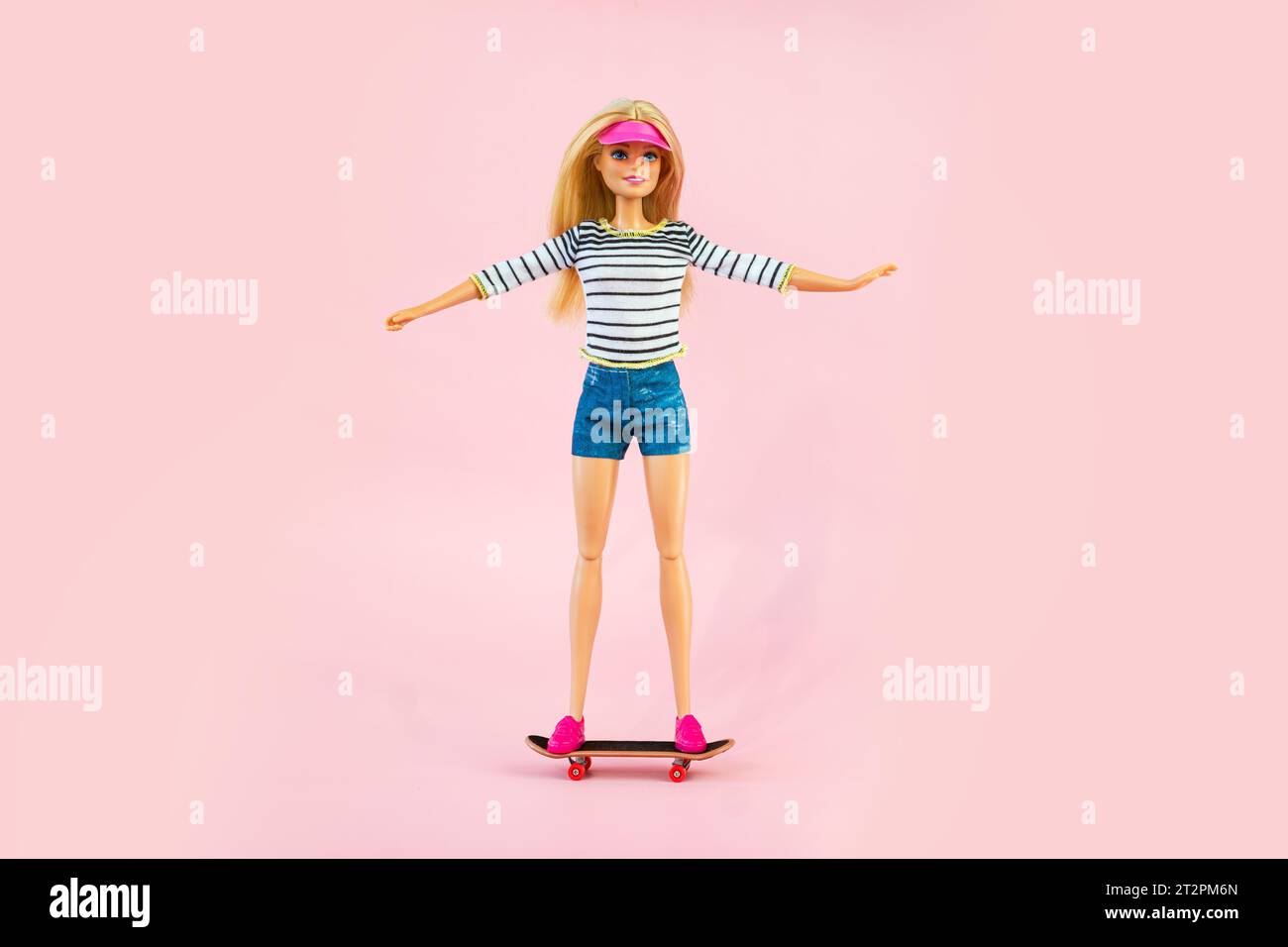 9 octobre 2023. Barnaul, Russie : poupée Barbie en vêtements de sport chevauchant un skateboard sur un fond rose Banque D'Images