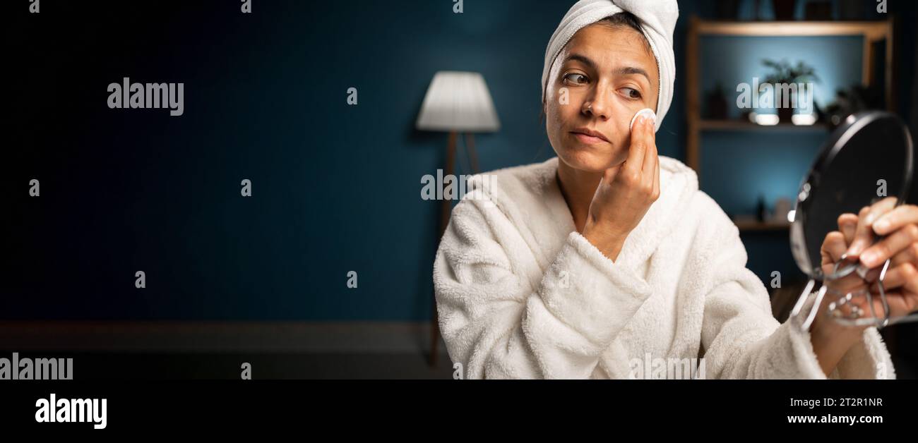 Femme hispanique utilisant un tampon de coton nettoyant le visage avec de l'eau micellaire prenant soin de la peau à la maison. Femme appréciant la routine de soin du visage. Bannière. Espace de copie Banque D'Images