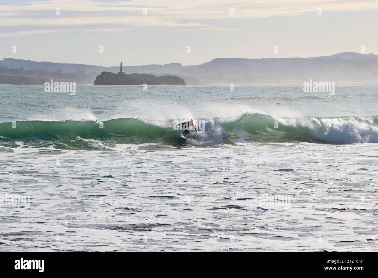 Un surfeur avec l'île de Mouro à l'entrée de la baie avec de fortes vagues sur un matin ensoleillé d'automne Sardinero Santander Cantabria Espagne Banque D'Images