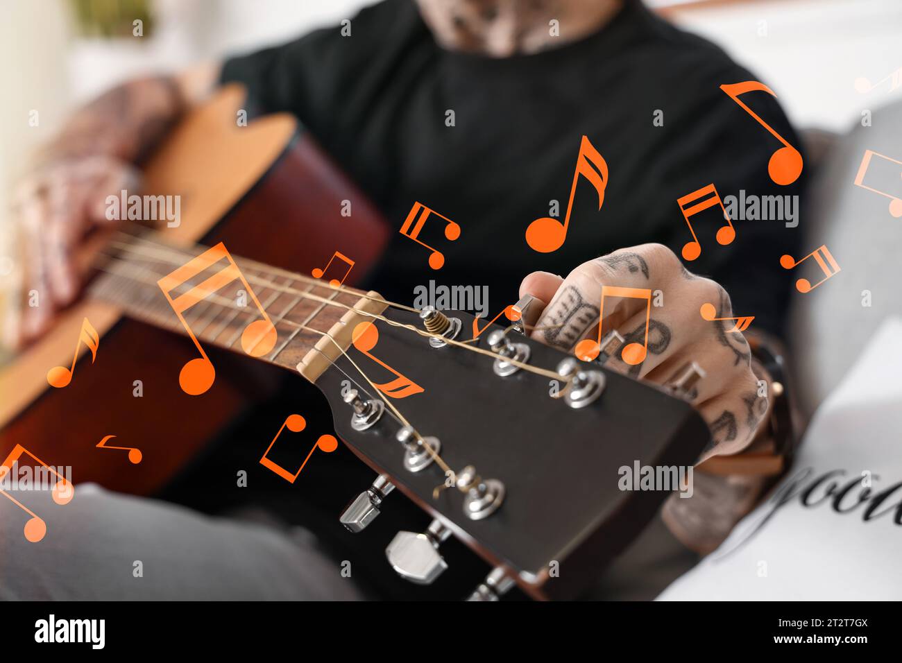 Jeune homme tatoué jouant de la guitare à la maison, gros plan Banque D'Images