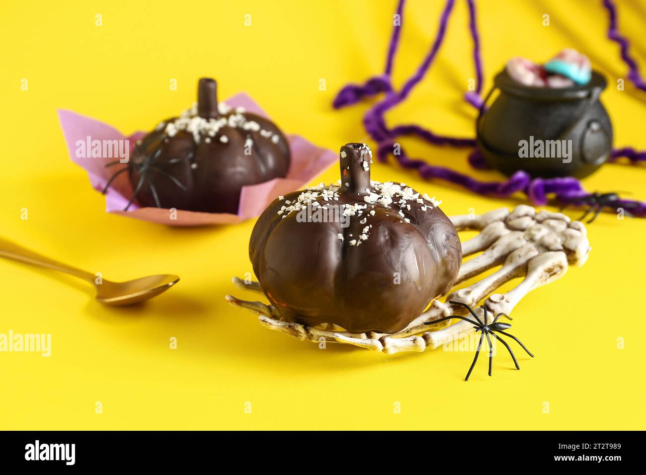 Délicieux gâteaux au chocolat, main squelette et araignée pour la célébration d'Halloween sur fond jaune, gros plan Banque D'Images