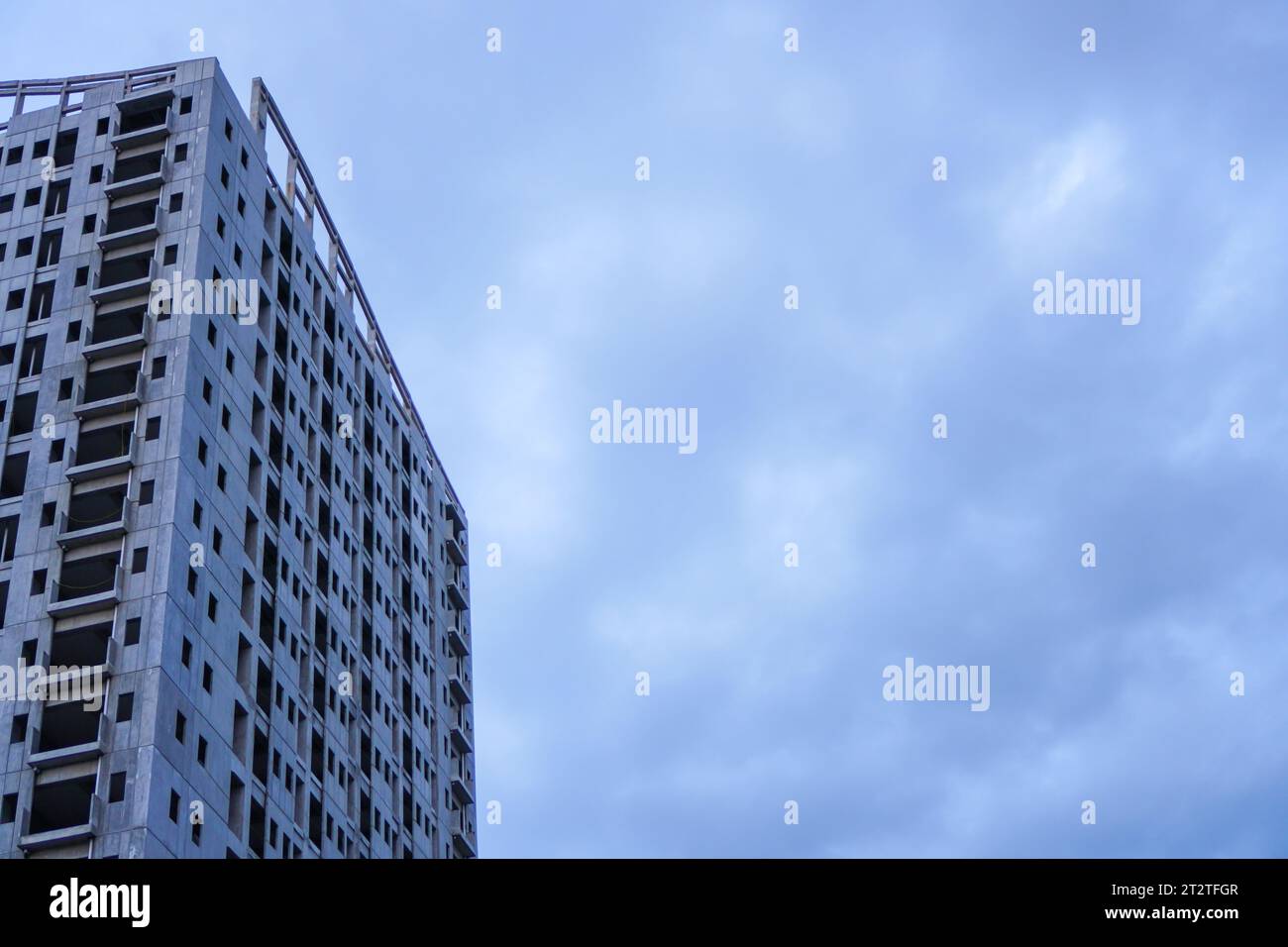 Un bâtiment inachevé se dresse devant un ciel gris sombre, dépourvu de tout signe de vie ou d'activité, avec ses espaces vides qui attendent d'être remplis Banque D'Images