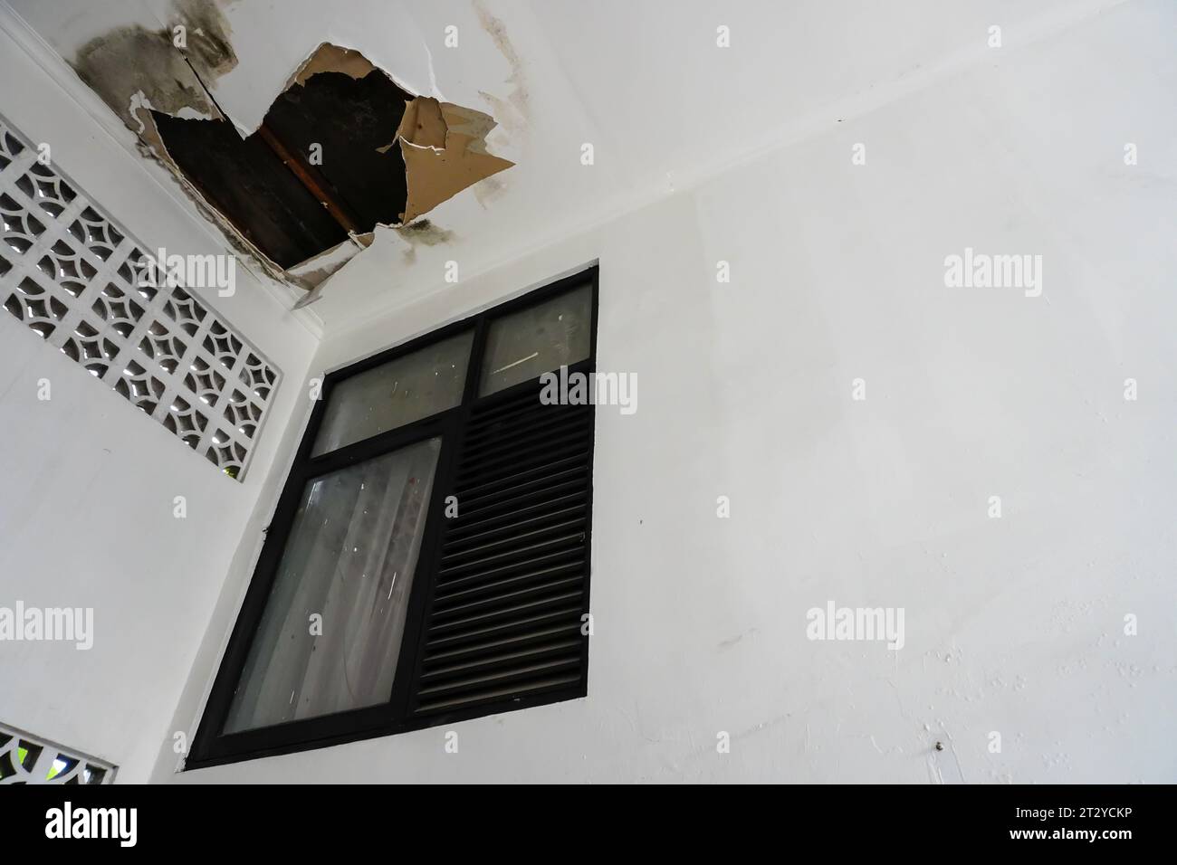 Plafond blanc endommagé causé par l'infiltration d'eau de pluie près de la fenêtre Banque D'Images