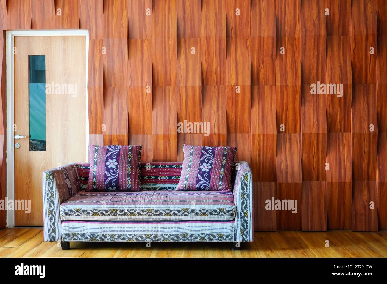 Canapé confortable motif batik près de la porte avec une toile de fond d'ornements muraux en bois texturé Banque D'Images