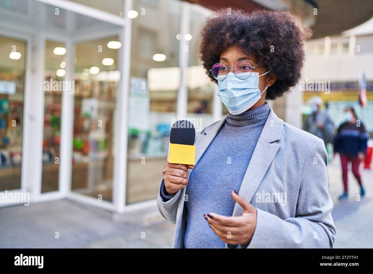 Femme afro-américaine journaliste portant un masque médical utilisant un microphone travaillant dans la rue Banque D'Images