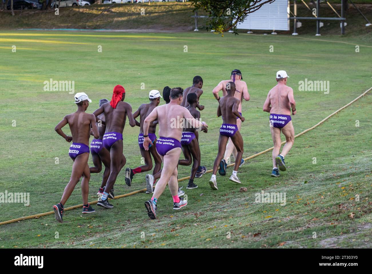 Les hommes multiraciaux, couvrant des générations, portent des speedos violets vibrants alors qu'ils courent passionnément pour soutenir la sensibilisation des hommes au cancer Banque D'Images