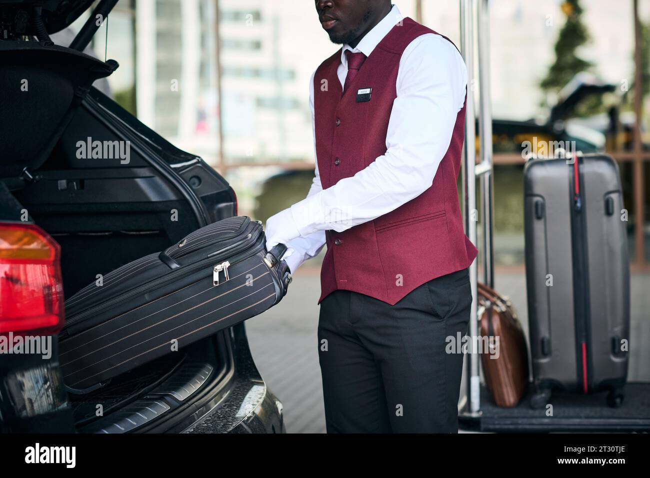 Portier afro-américain prenant des bagages de la voiture et le mettant sur le chariot Banque D'Images