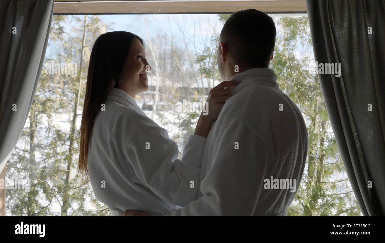 L'homme et la femme aimant s'étreignent le matin dans la chambre contre la fenêtre. Action. Mari et femme près de la fenêtre avec des arbres derrière. Banque D'Images