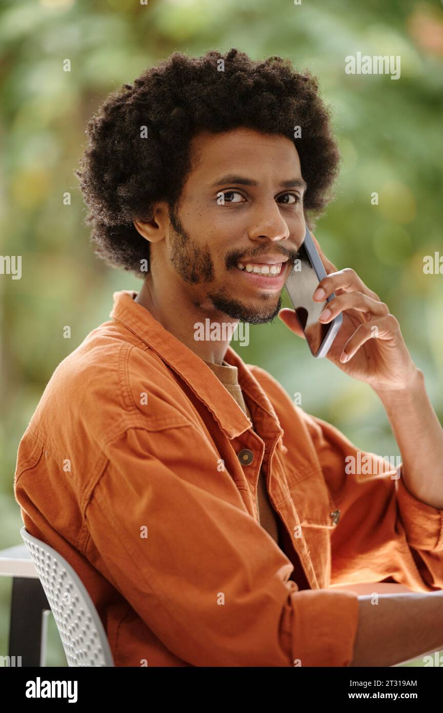 Portrait de souriant Noir homme parlant au téléphone et regardant la caméra Banque D'Images