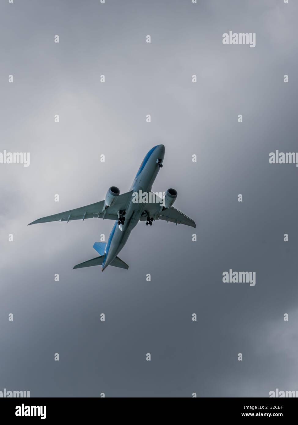 Un avion se préparant à atterrir contre un ciel nuageux - vue du dessous de l'avion avec le train d'atterrissage abaissé Banque D'Images