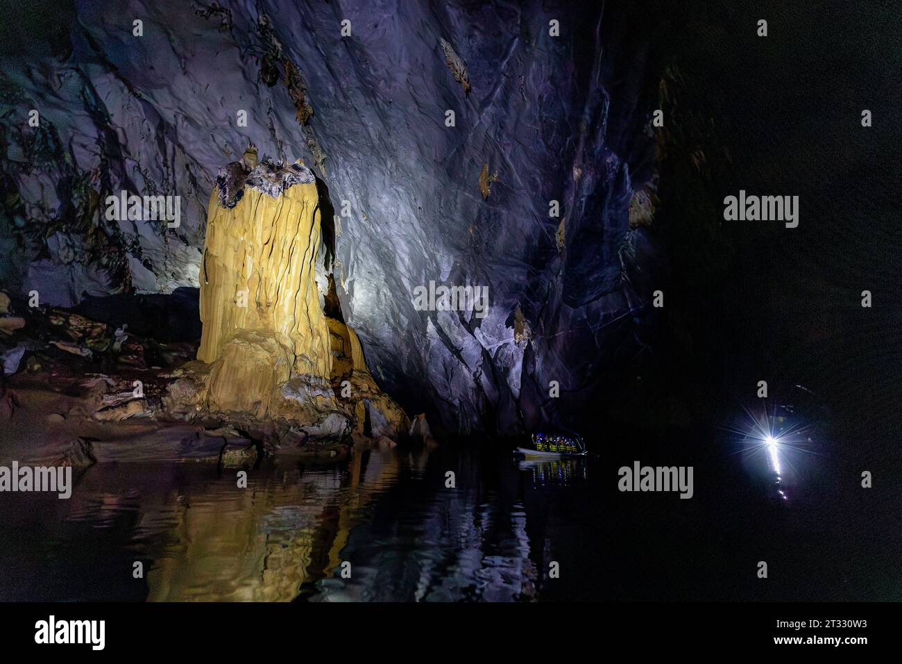 Les touristes explorent les grottes souterraines sombres de la rivière en bateau et observent les formations rocheuses en utilisant des lampes frontales Banque D'Images