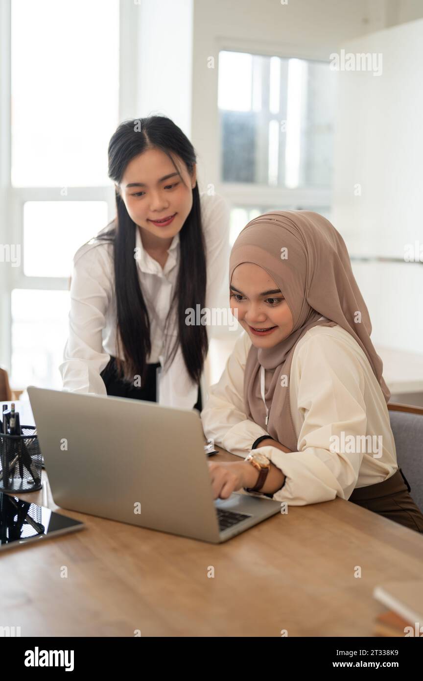 Une belle et professionnelle femme d'affaires asiatique-musulmane utilisant son ordinateur portable tout en discutant de travail avec son collègue dans la salle de réunion. Entreprises diverses Banque D'Images